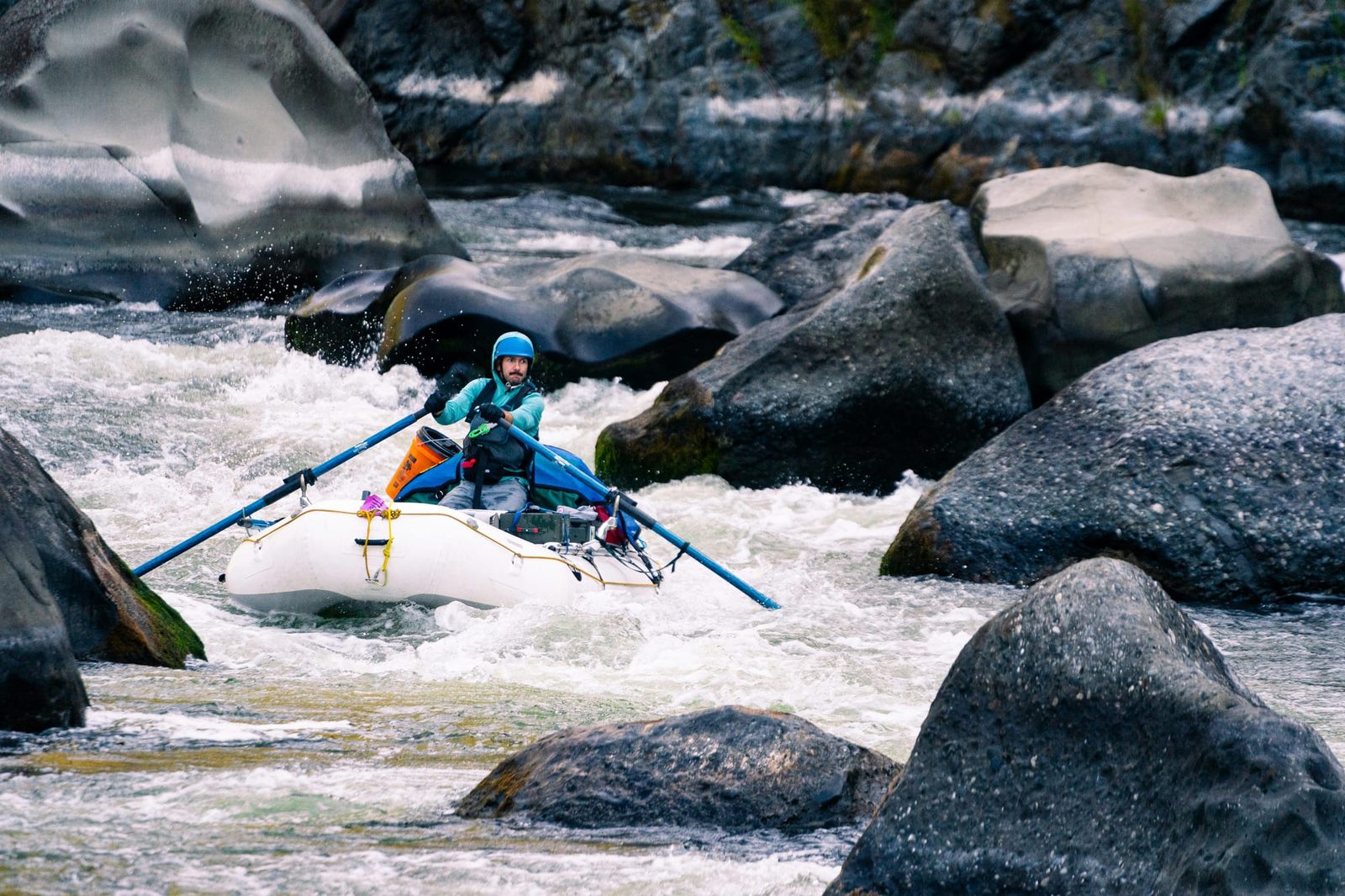 A rafter paddling through whitewater between large boulders